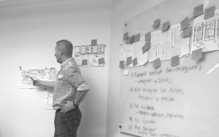 Web design services. A web designer points to a user flow diagram pinned to a wall. Web design services. A web designer points to a user flow diagram pinned to a wall.